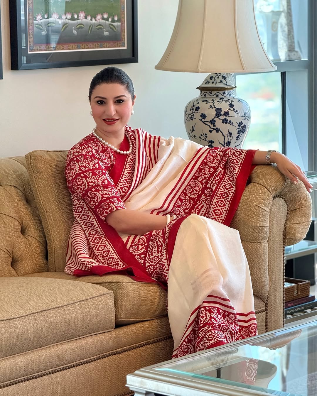 Woman wearing a red and white block print saree sitting on a beige couch indoors